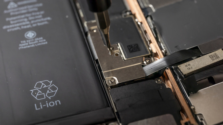A screwdriver initiating repairs inside a smartphone next to a lithium-ion battery.