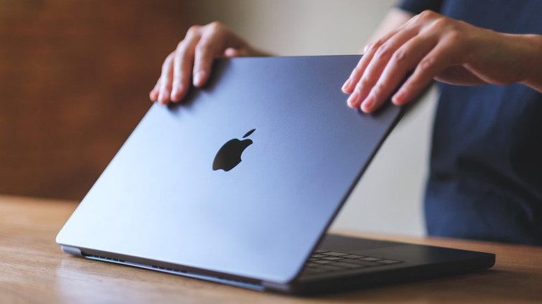 A person opening a MacBook on a desk
