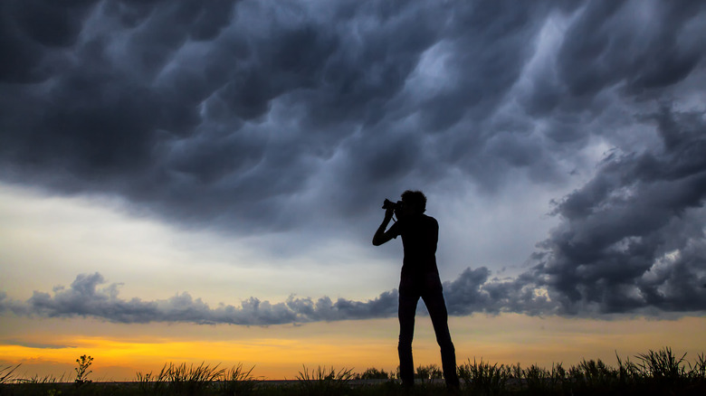 A person taking photos of a cloudy sky.