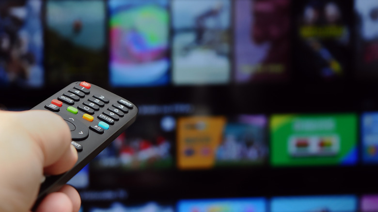 A person using a remote to change the channel on a TV that is blurred in the background