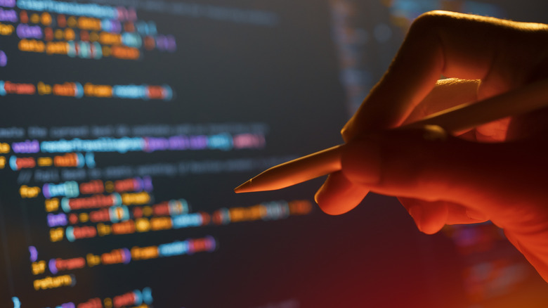 Hand holding stylus in front of computer screen covered in code