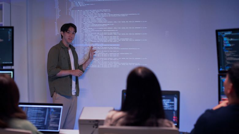 Teacher standing in front of a screen, showing code to students