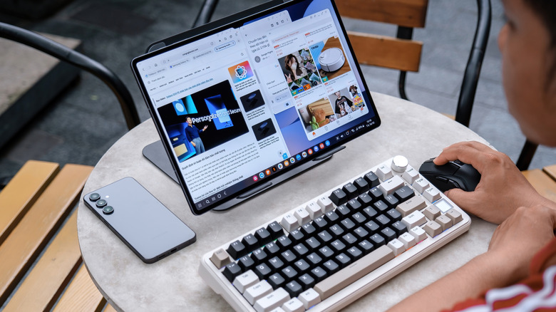 A person in an outdoor cafe using a propped-up Samsung Galaxy tablet as a computer connected to a keyboard and a mouse