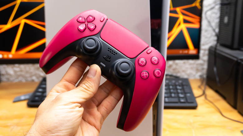 PlayStation 5 DualSense controller in red in front of PS5 console and desk.