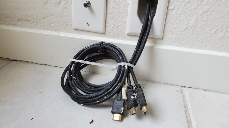 A bundle of HDMI cables poking out of a cable pass-through at the bottom of a stud bay.