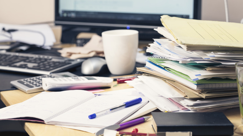 A messy desk covered in papers, folders, pens, and a coffee cup