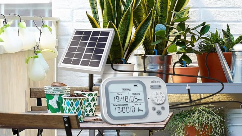 An indoor photo of the Beday Solar Automatic Drip Irrigation System, both the solar panel and the control center are surrounded by a number of potted plants