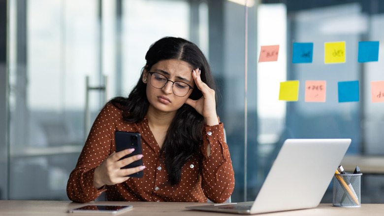 a businesswoman in an office looking frustrated with her phone