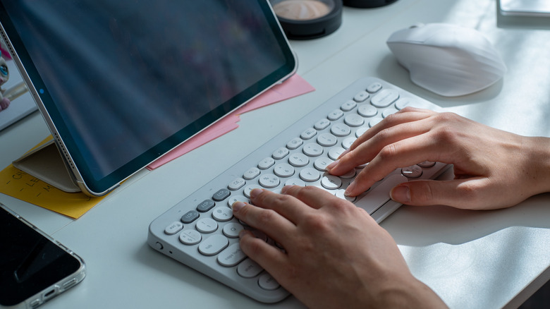 Top down view of someone using a wireless keyboard and mouse with a tablet.