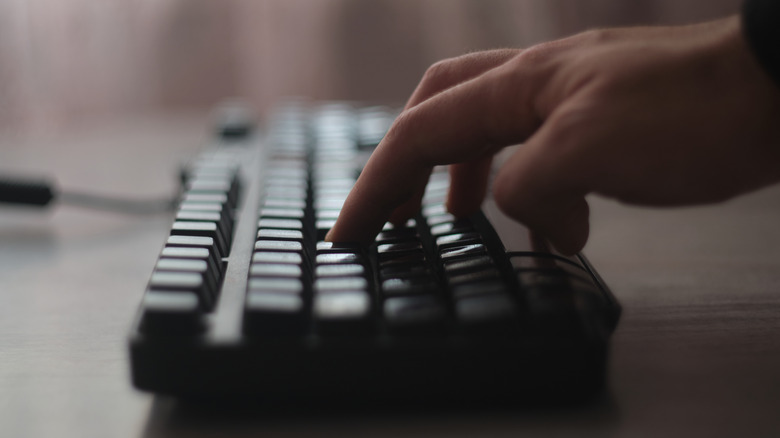 A side view of a wired mechanical keyboard in use with someone typing.