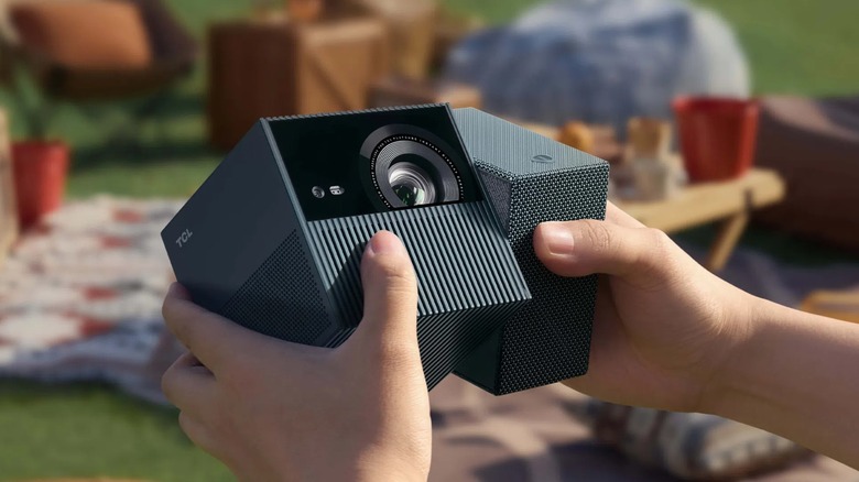 A photo showing a closeup of a black TCL PlayCube nestled between an individual's hands, the device is turned in such a way to show that it the projector itself can be rotated