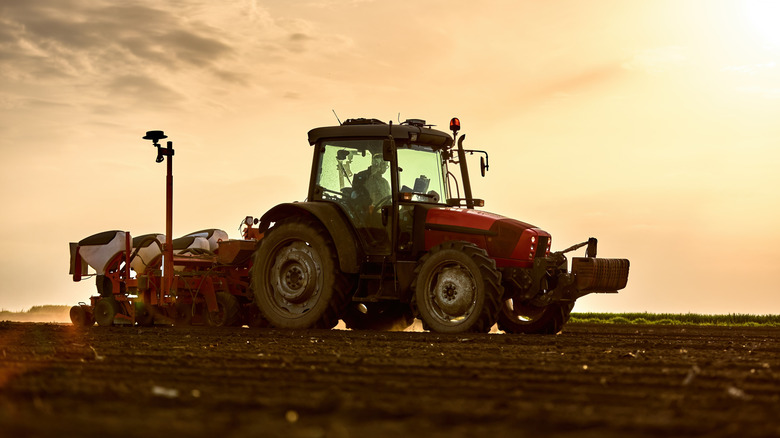 A farmer uses heavy machinery to spread fertilizer on cropland