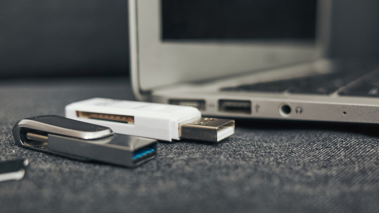 A laptop with two USB sticks next to it.