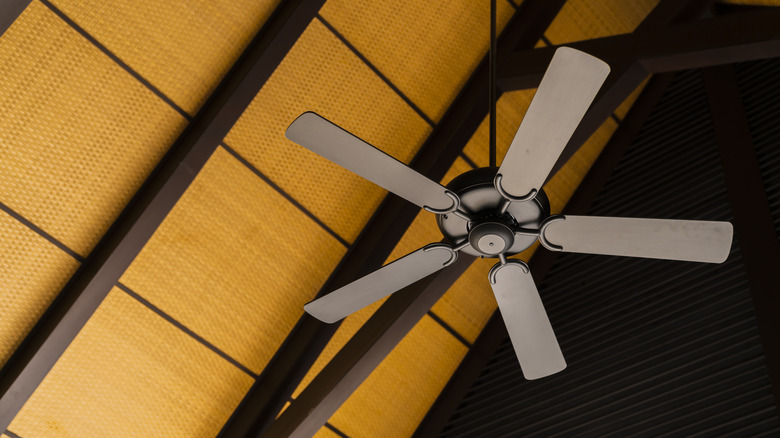 A dark ceiling fan hanging below a wooden ceiling