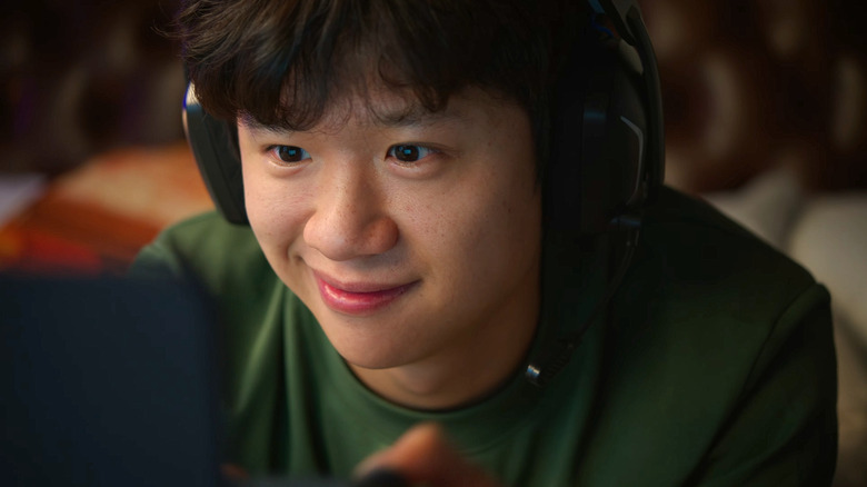 A close up of a happy young man's face, he's playing a game on a device and wearing a gaming headset