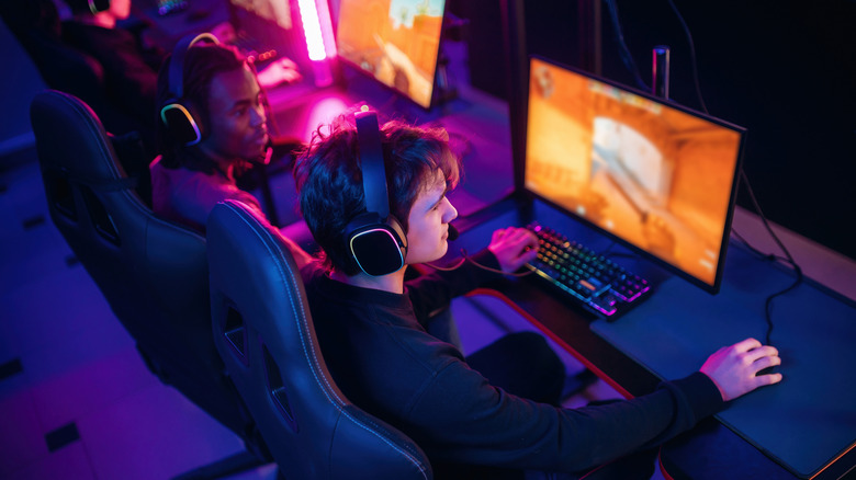 Row of people playing a shooter game on PCs in a dim room
