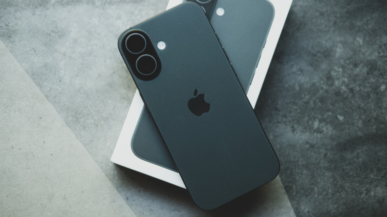 A black iPhone sitting on top of its own packaging, both objects sit on what appears to be a marble counter