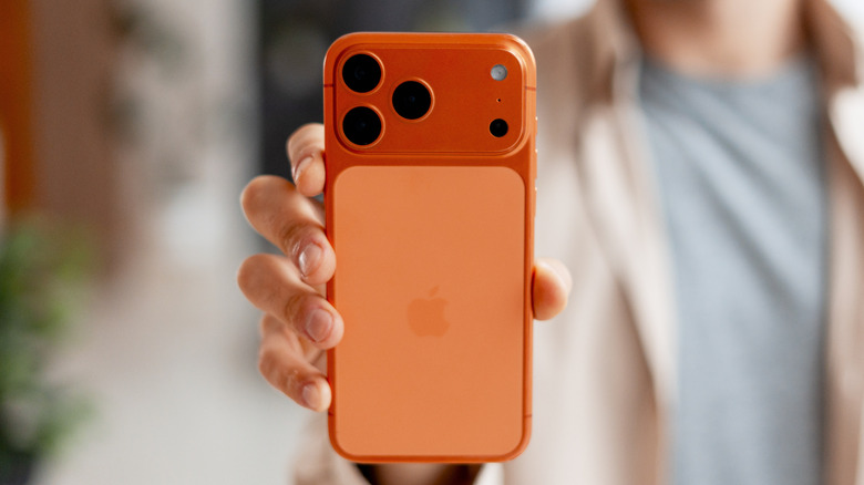 An individual holding a Cosmic Orange iPhone 17 Pro, the image focuses on the device in the person's hand