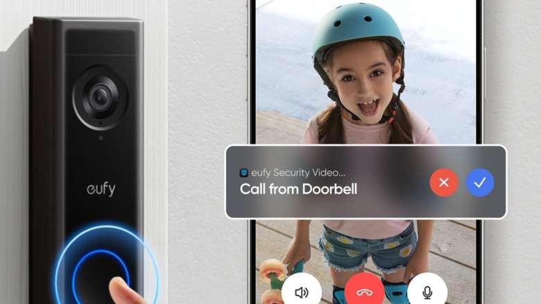 The Eufy Video Doorbell C31 mounted to an exterior door frame. Next to it is a smartphone showing the Eufy app opened to a live feed.