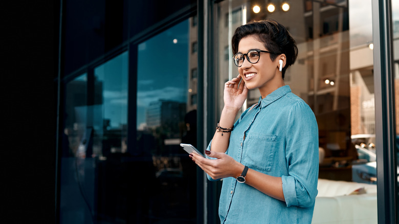 a woman standing on a city street listening to wireless earbuds