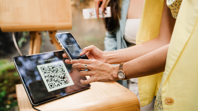 Hands holding a phone used to scan a QR code on a tablet