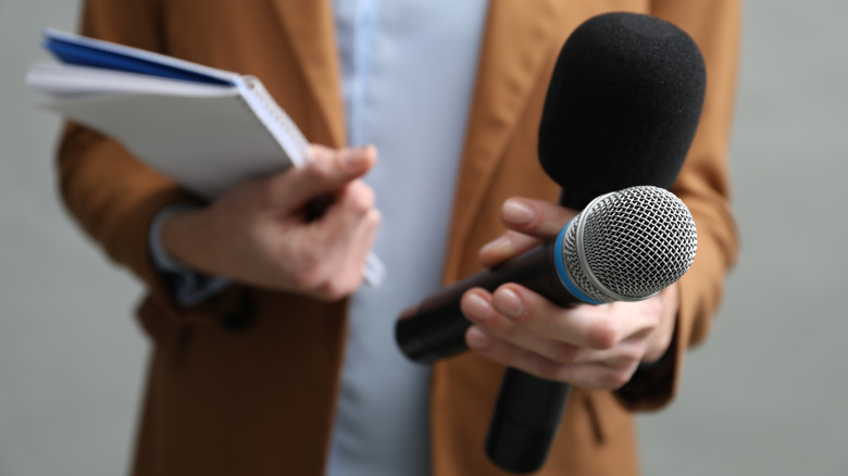 A journalist holds a notepad and two microphones