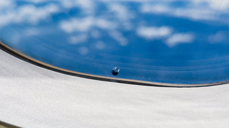 bleed hole in the window of an airplane, sky and clouds visible outside