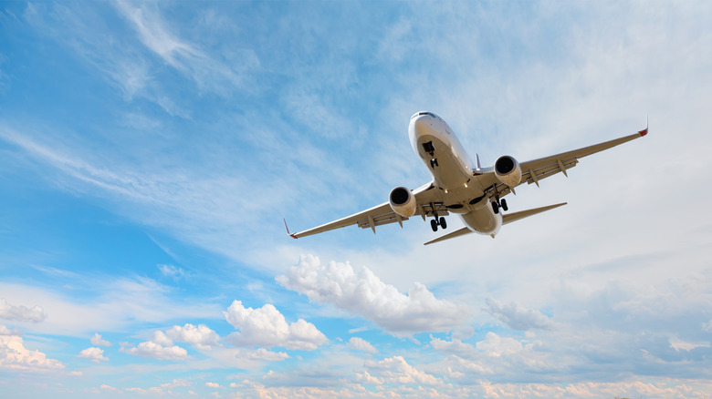 large airplane flying through the sky, landing gear retracting, clouds and sky visible in background