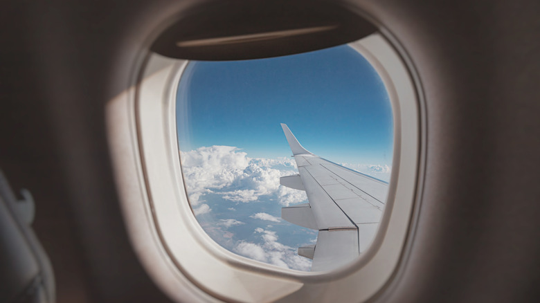 looking out an airplane window, the wing visible above the clouds