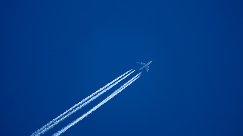 aircraft with contrail forming behind it across a blue sky