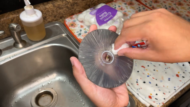 Person cleaning scratched disc using cotton balls and toothpaste