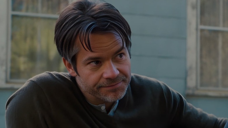 Henri (Timothy Olyphant) sitting down in 