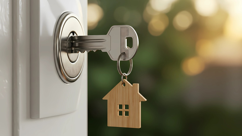 A key being held inside a door lock; the key is on a keychain with a wooden symbol of a house