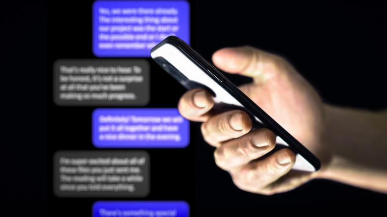 A person holding a smartphone with a text conversation proceeding in the background