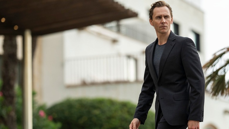 Tom Hiddleston walks menacingly through a luxury hotel.