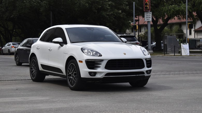 A portrait of a white colored Porsche Macan SUV cruising in a downtown district
