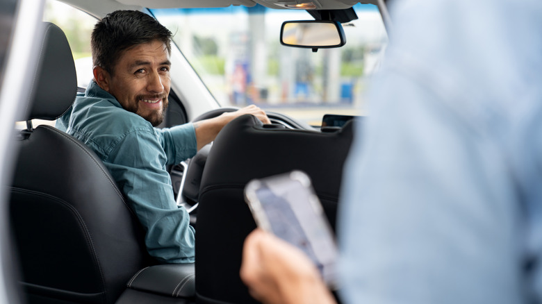 A rideshare driver picking up a passenger and smiling.