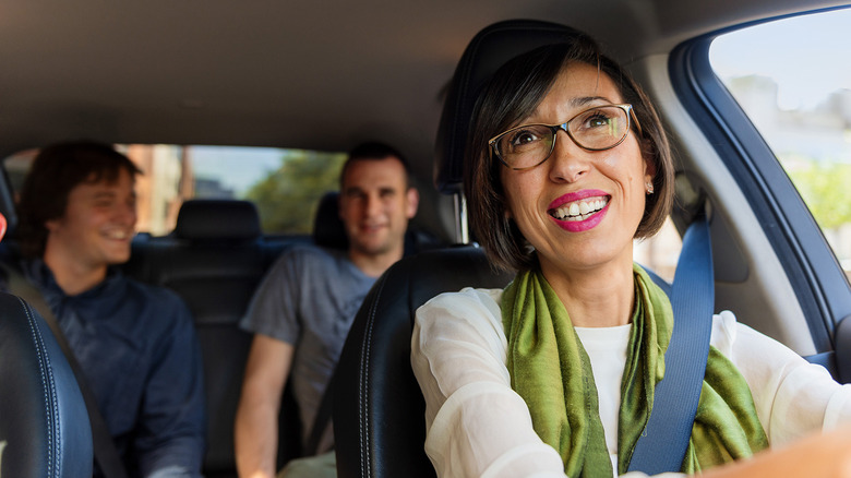 A female Uber driver looks at two male passengers from her rearview mirror.