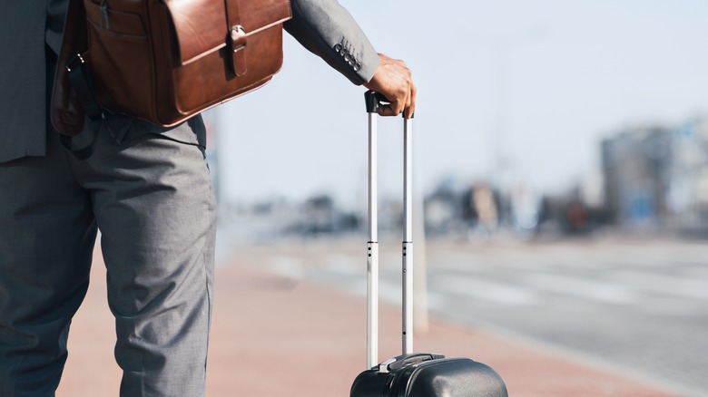 The back of a man on the street with a suitcase.
