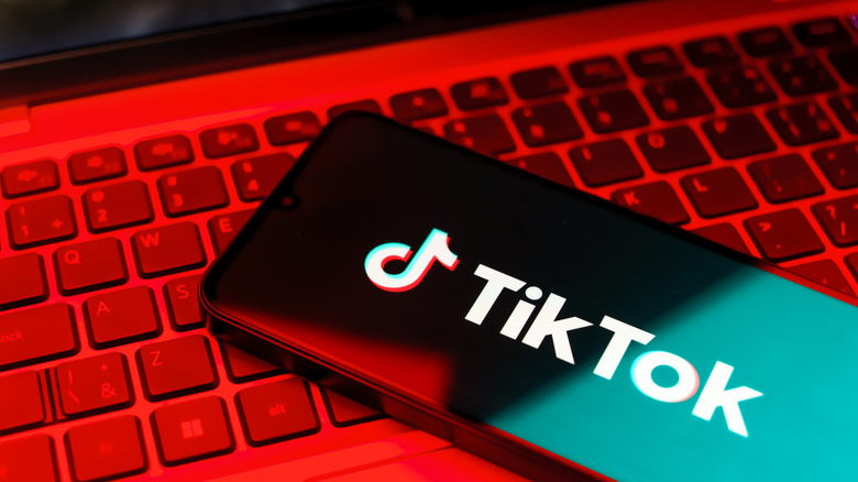 A phone displaying the TikTok logo and label lying on top of a laptop keyboard under a red light