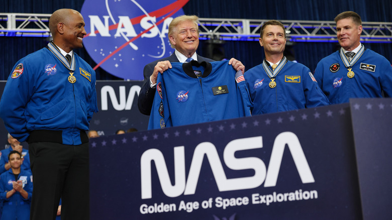 President Trump holds up a NASA uniform while accompanied by members of the Artemis II crew