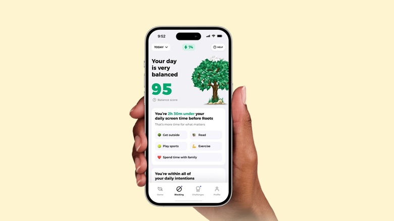A hand holding an iPhone with the Roots app opened