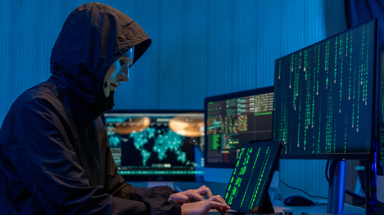 A masked hacker launching a cyberattack using multiple devices
