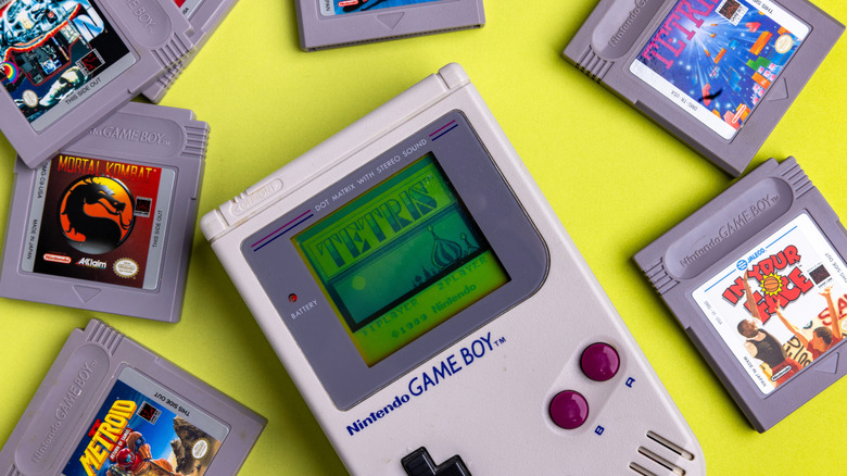An original Game Boy system sitting on a yellow surface with game cartridges around it