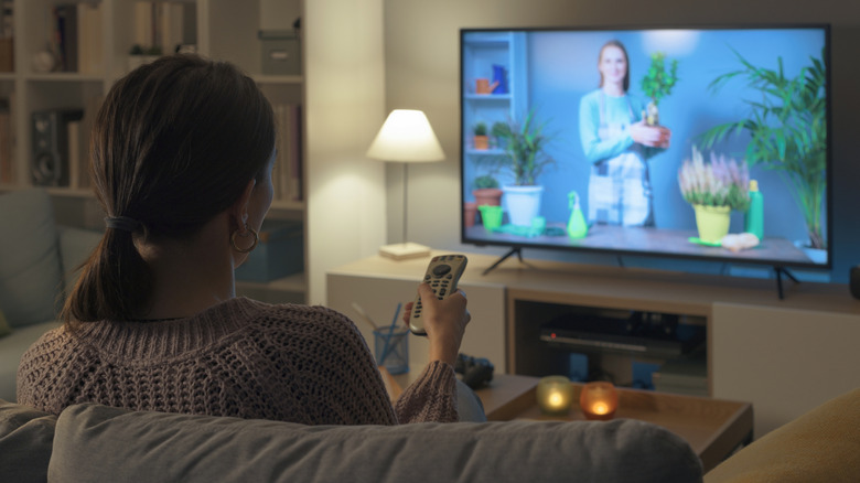 A woman holds a remote while watching a program on her TV.