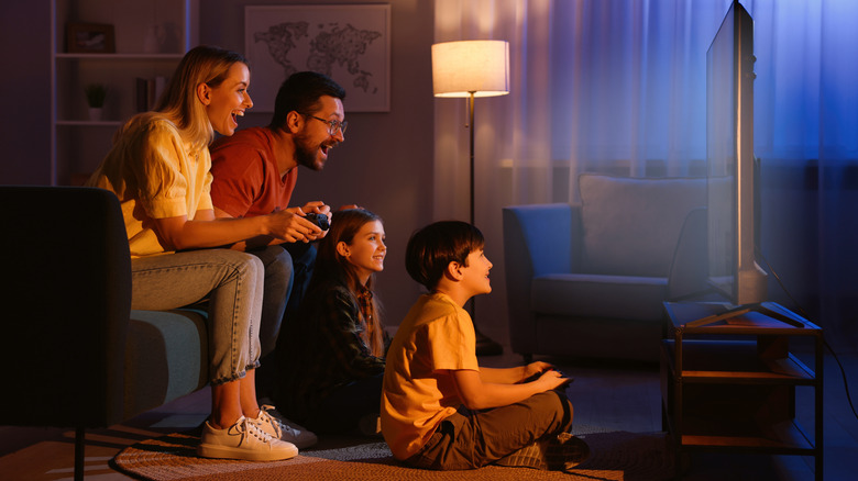 A family sitting in a living room, playing a videogame with controllers on a TV