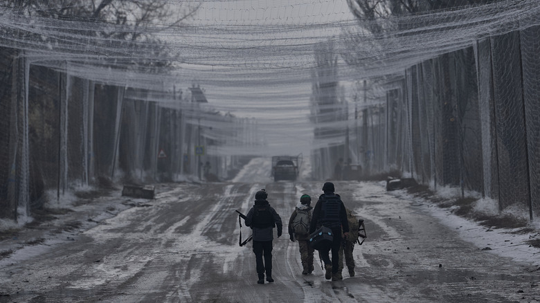 A group of Ukrainian soldiers walk down a snowy road beneath a netted canopy designed to prevent drones from attacks civilian and military transports.
