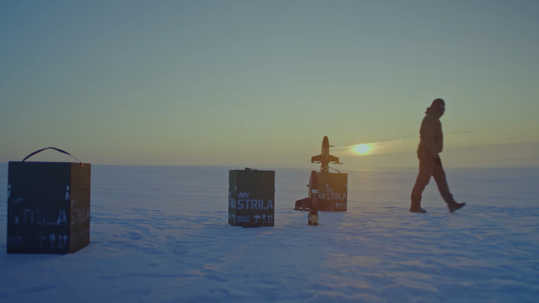 A man walks across an arctic landscape at sundown, turning away from three crates of Strilla interceptors, where two of the rocket-boosted quadcopters are visible.