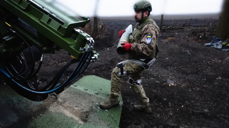 A soldier loads a CAESAR self-propelled Howitzer while wearing the exoskeleton, which video editors highlight around his legs an waist.
