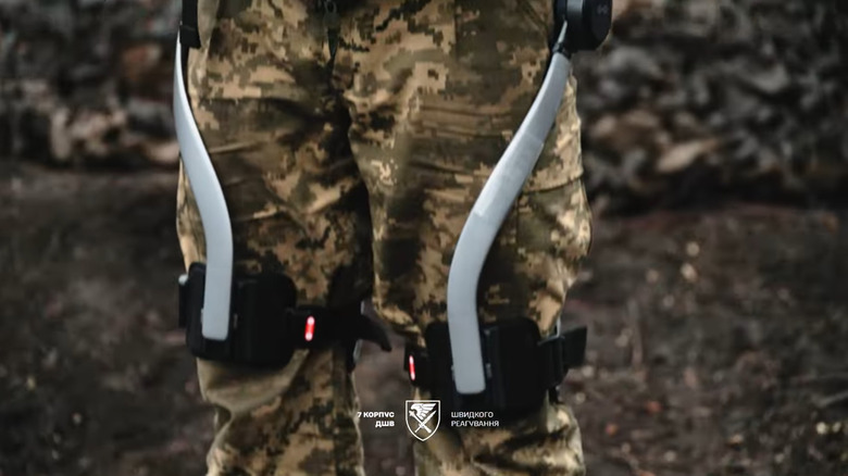 A close up shows the silver exoskeleton wrapped around a soldier's legs.